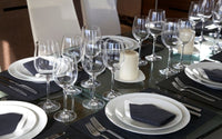 Table avec une nappe grise foncée, des assiettes blanche, de beaux verre à pieds, des bougies et des serviettes grise foncées sur les assiettes.