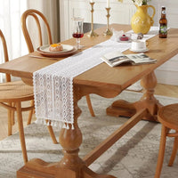 Chemin de Table Blanc en Macramé Style Vintage sur une table en bois avec des assiettes, un verre, des bougies, un pot de fleur, un magazine et une tasse