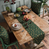 Chemin de Table Vert de Noël Raffiné et Design sur une table en bois avec des assiettes, des couverts, des plantes et de la décoration