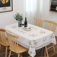 Nappe Blanche Sophistiquée à Motif Floral sur une table avec des assiettes, des couverts, un verre, une bouteille et des fleurs