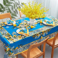 Nappe bleu imperméable avec motifs citrons et feurs, dans une salle à manger avec les couverts et plante sur la table.