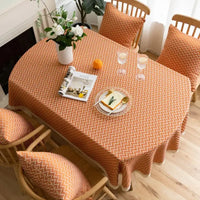 Nappe de table ovale orange avec motif design sur une table avec une assiette, des couverts, des verres, des fleurs, un magazine, un fruit et des chaises autour de la table